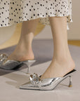 Silver high-heeled shoes worn with a polka dot skirt on a neutral background