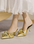 Gold high-heeled shoes worn with a white skirt on a neutral background