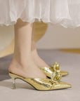 Gold high-heeled shoes with decorative elements worn with a white skirt.