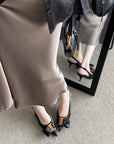Person wearing a beige skirt and black high-heeled shoes with gold accents, standing in front of a mirror.