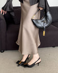 Person wearing a beige skirt, black top, and black high-heeled shoes, holding a black handbag.