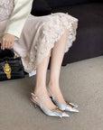 Person wearing silver high-heeled shoes with a lace skirt and black handbag on a gray carpet.
