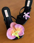 Black high-heeled sandals with pink orchids on a wooden surface