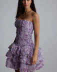 Woman wearing a purple strapless 3d floral dress with floral patterns against a plain background