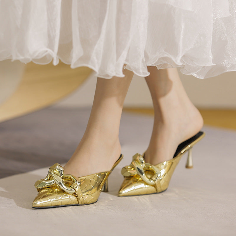 Gold high-heeled shoes worn with a white skirt on a neutral background