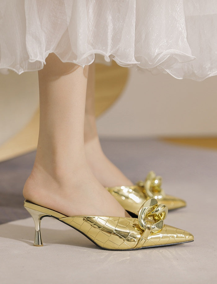 Gold high-heeled shoes with decorative elements worn with a white skirt.