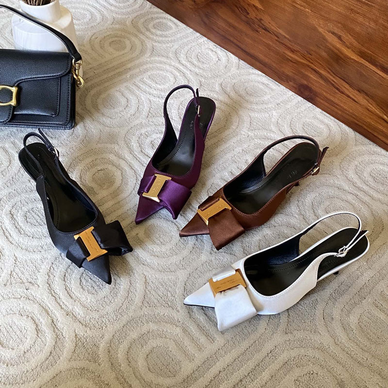 Four pairs of high-heeled shoes in black, purple, brown, and white on a textured surface.