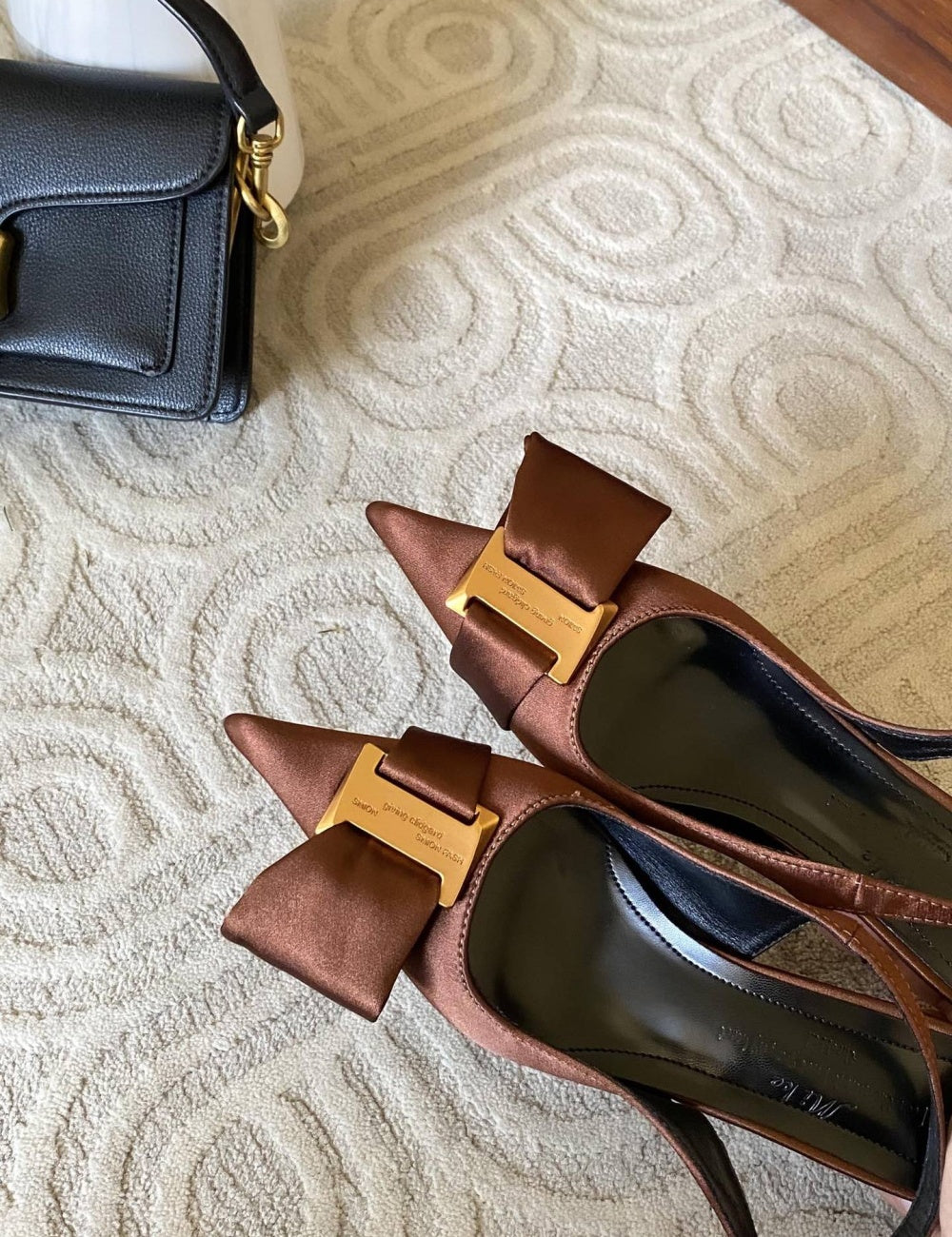 Brown high-heeled shoes with gold buckles on a textured surface