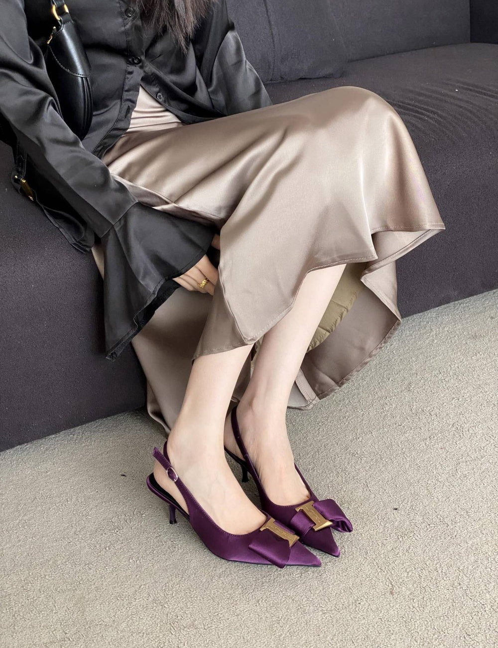 Person wearing a coat and beige skirt with purple high-heeled shoes sitting on a couch.