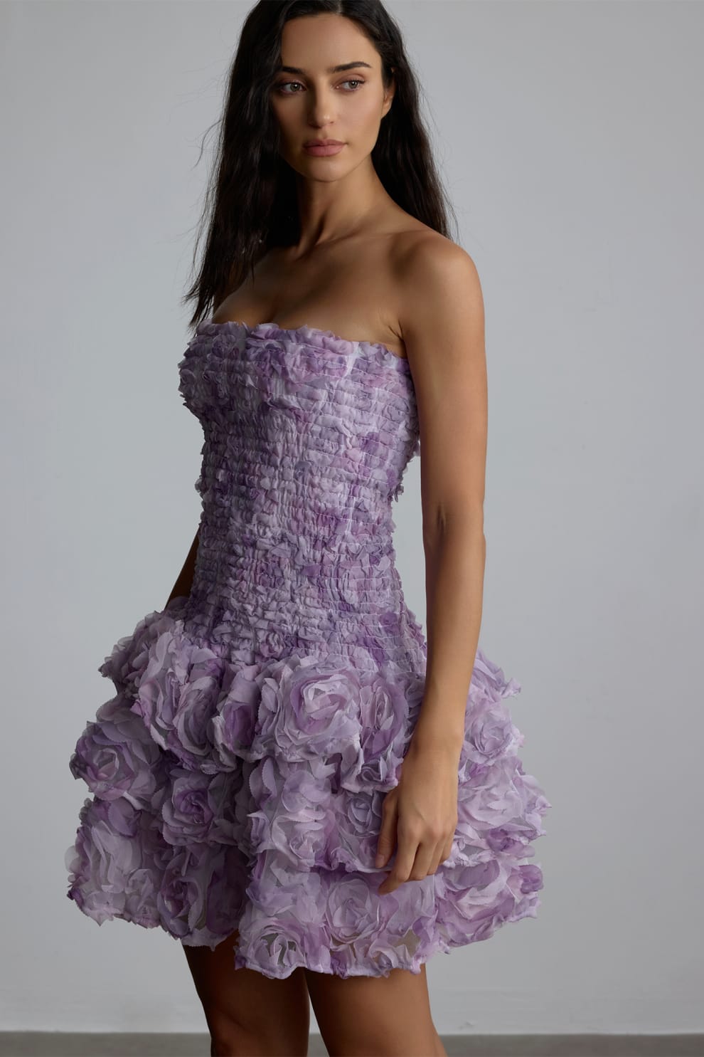 Woman wearing a purple strapless 3d floral dress with floral patterns against a plain background