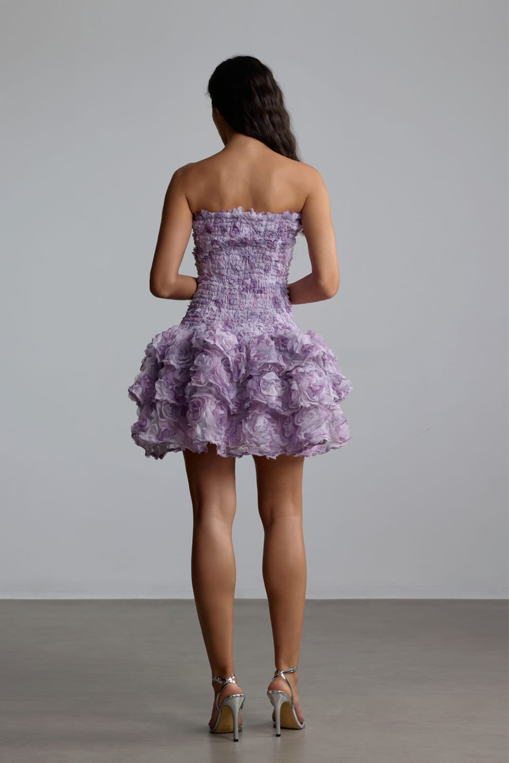Woman wearing a purple strapless 3d floral dress with floral patterns against a plain background